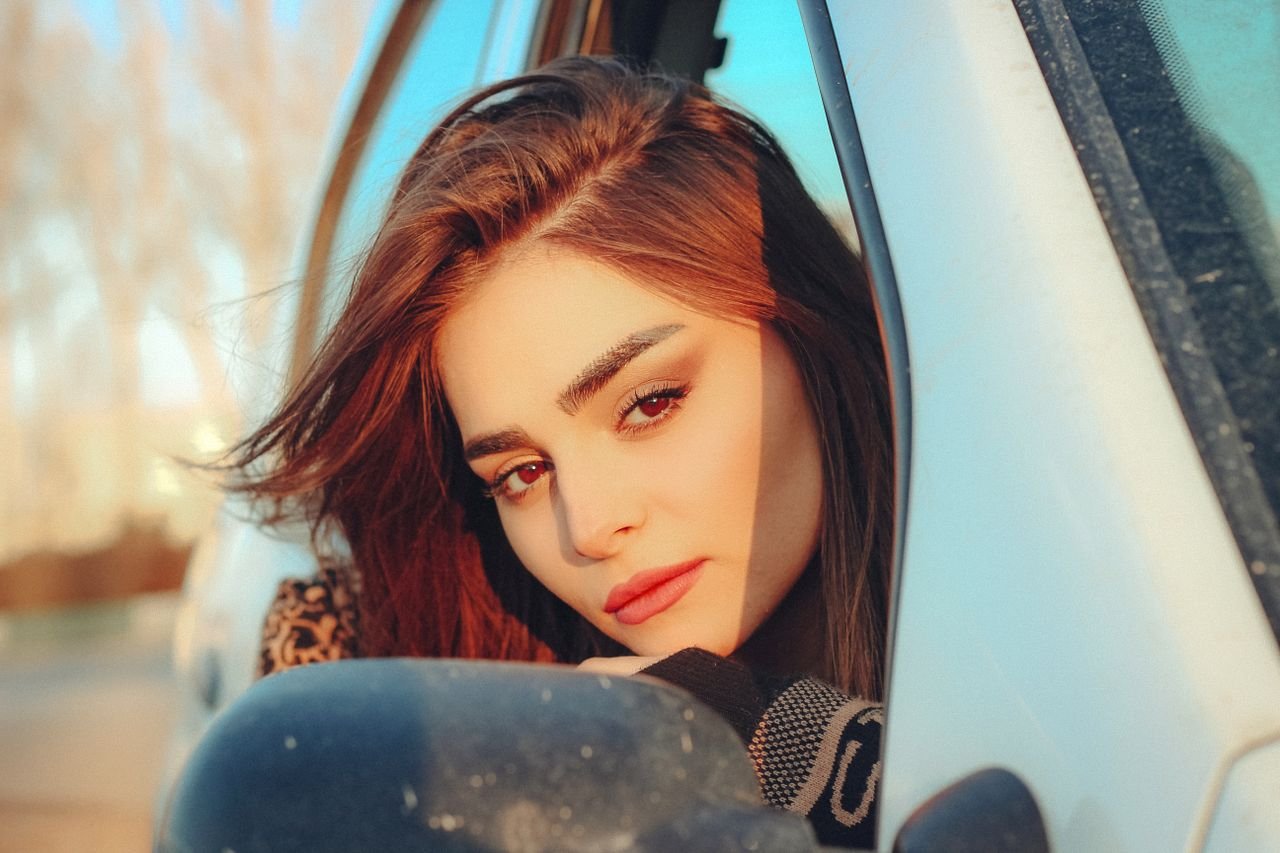 Young woman gazing through car window in Tehran with thoughtful expression.