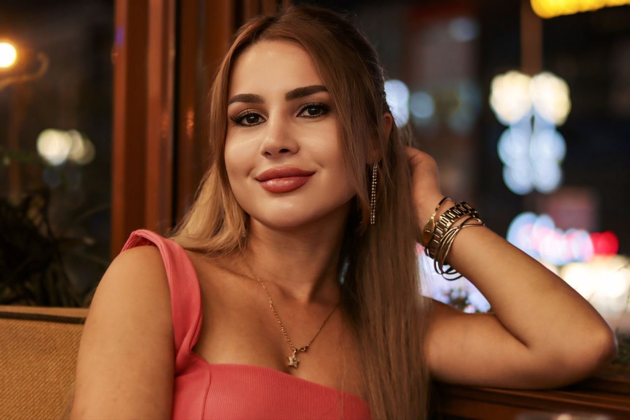 Stylish woman posing elegantly in evening attire indoors, with a soft focus background.
